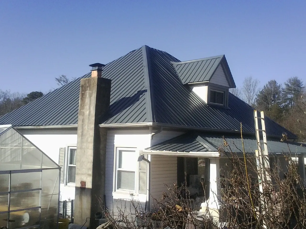 Dark blue standing seam metal roof on a white farmhouse with dormer — Slate & Tile Roof Repair by Roofing Brothers in Rebecca