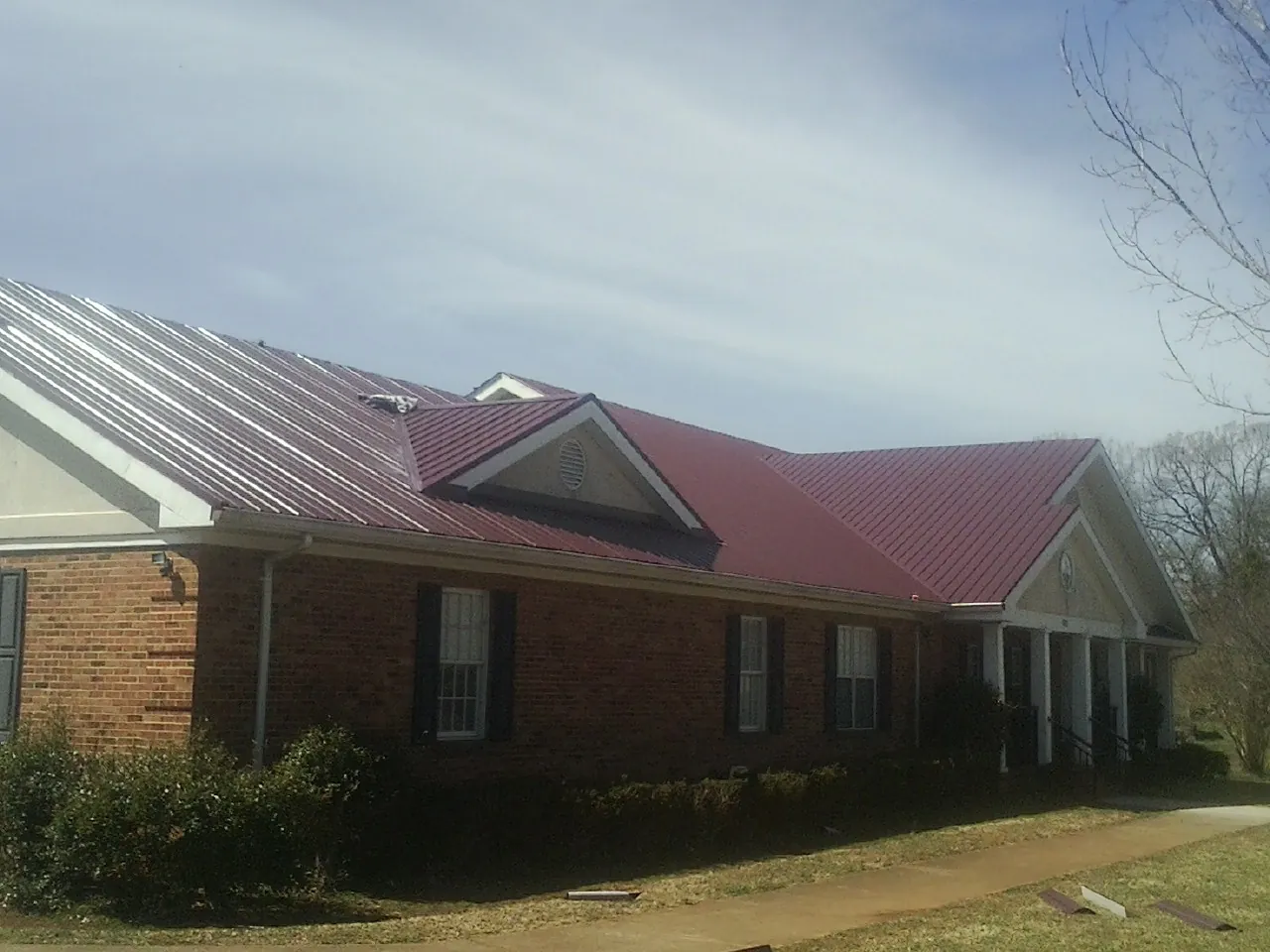 Red metal roof with gabled entries on a long brick building, from a Hail Damage Roof Repair job in Rebecca