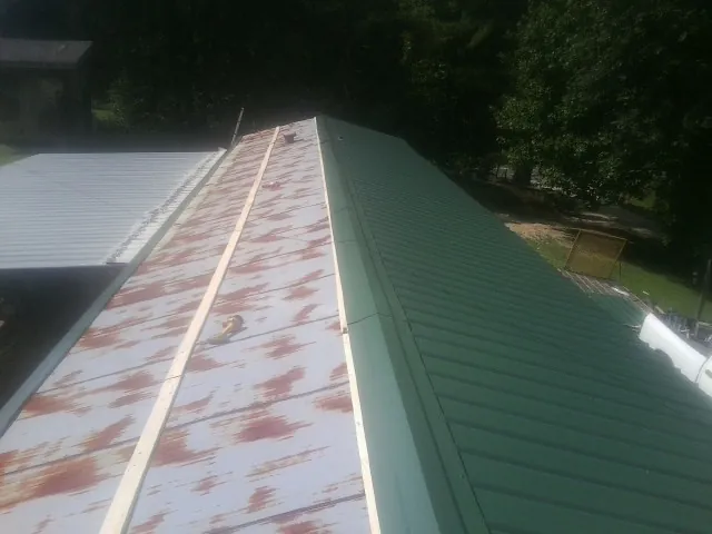Old rusted panels beside newly installed green metal roofing — Wind Damage Roof Repair by Roofing Brothers in Rebecca