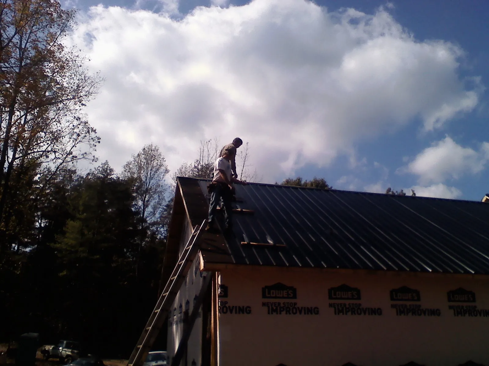 Roofer fastening dark metal panels high against a cloudy sky, from a Roof Inspection job in Rebecca