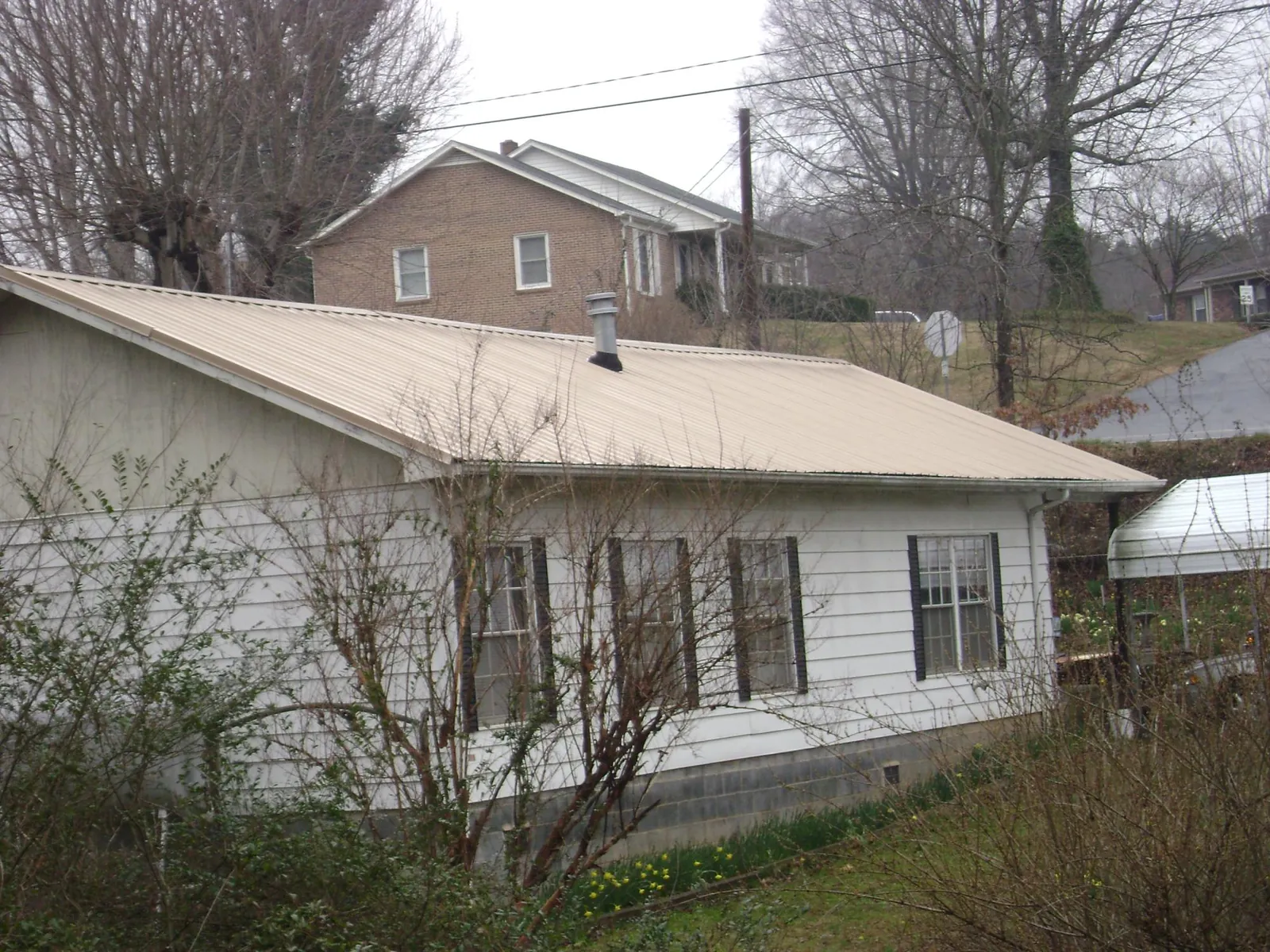 Tan metal roof on a white sided house set into a hillside — Commercial Roofing by Roofing Brothers in Rebecca
