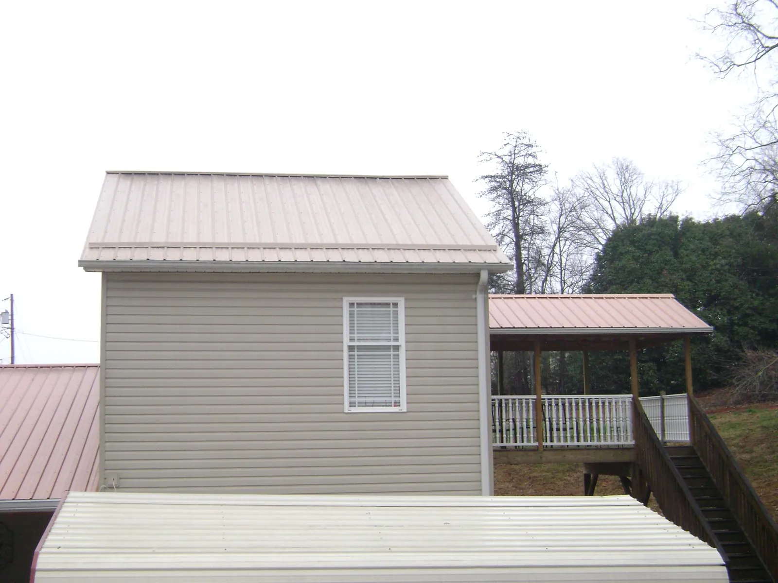 Tan metal roofs on a two story addition and attached porch, from a Roof Replacement job in Rebecca